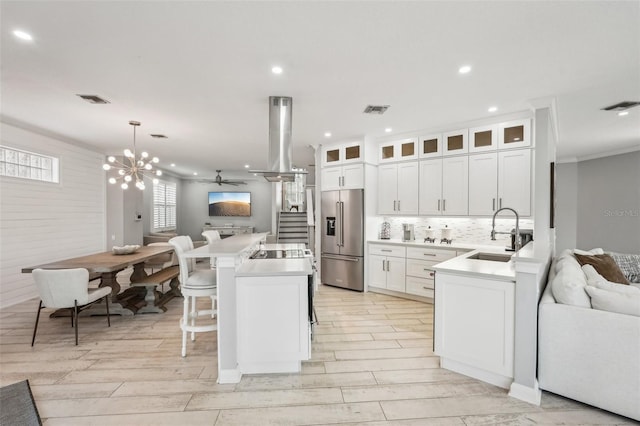 kitchen with high end refrigerator, a sink, open floor plan, island exhaust hood, and glass insert cabinets