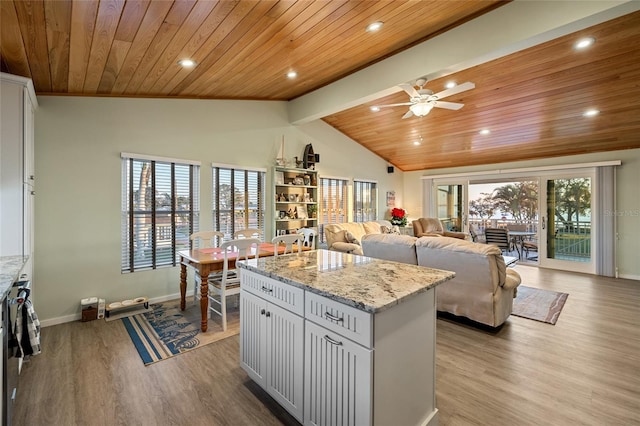 kitchen with white cabinetry, a kitchen island, light stone counters, and light wood-type flooring