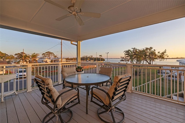 deck at dusk with a water view and ceiling fan