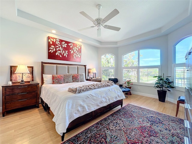 bedroom with ceiling fan, light wood-type flooring, and a tray ceiling