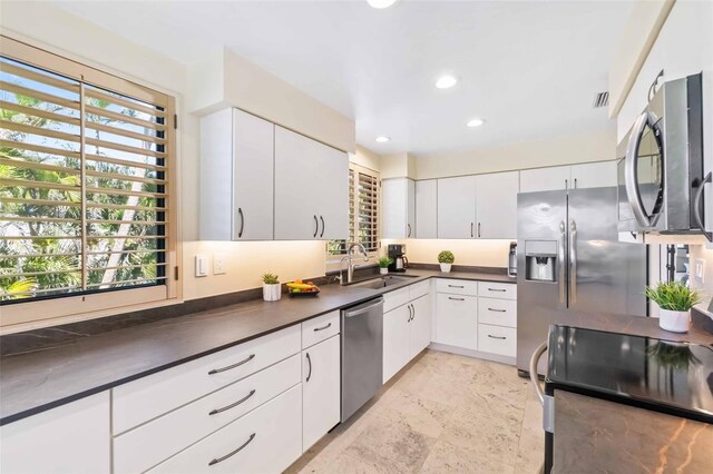 kitchen with white cabinets, dark countertops, appliances with stainless steel finishes, a sink, and recessed lighting