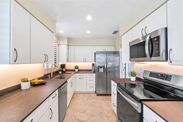 kitchen featuring dark countertops, white cabinetry, stainless steel appliances, and a sink