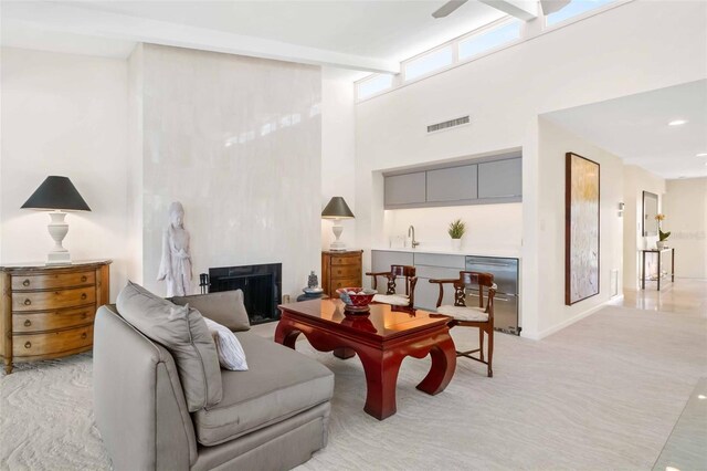 living area featuring light carpet, a fireplace, visible vents, a towering ceiling, and beam ceiling