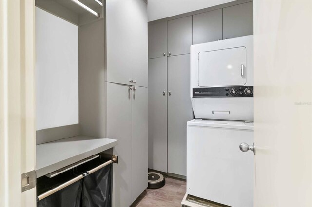 clothes washing area with stacked washer / dryer, cabinet space, and light wood-style flooring