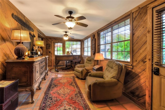 living area with tile patterned floors, ceiling fan, and wooden walls