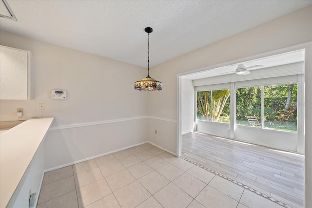 unfurnished dining area featuring ceiling fan, light tile patterned floors, and a textured ceiling