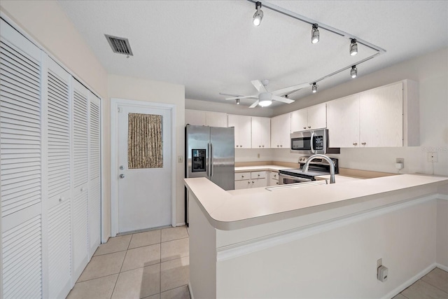 kitchen with kitchen peninsula, a textured ceiling, stainless steel appliances, ceiling fan, and light tile patterned floors