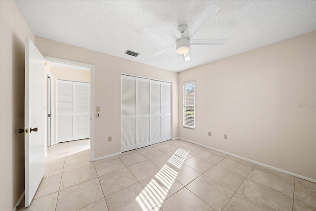 unfurnished bedroom with ceiling fan, light tile patterned flooring, a textured ceiling, and a closet