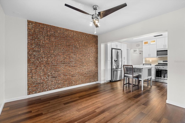 dining space featuring dark hardwood / wood-style floors, ceiling fan, and brick wall