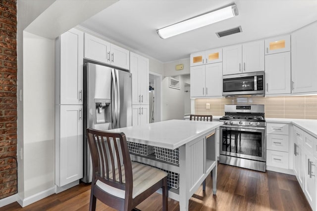 kitchen featuring white cabinets, appliances with stainless steel finishes, dark wood-type flooring, and brick wall