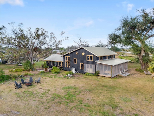 rear view of property featuring a sunroom, a fire pit, and a lawn