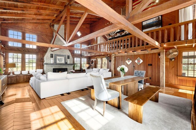 living room with wooden walls, high vaulted ceiling, a wealth of natural light, and a brick fireplace