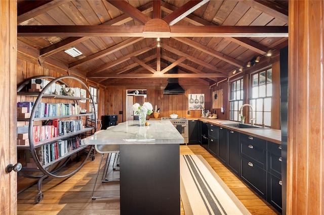 kitchen with light wood-type flooring, high end stove, wall chimney range hood, sink, and a center island