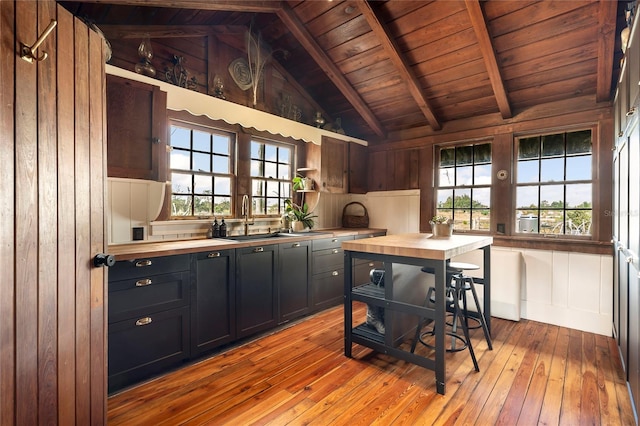 kitchen featuring vaulted ceiling with beams, plenty of natural light, light hardwood / wood-style floors, and wooden walls