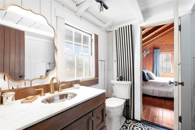 bathroom featuring vanity, wooden walls, lofted ceiling with beams, hardwood / wood-style floors, and toilet