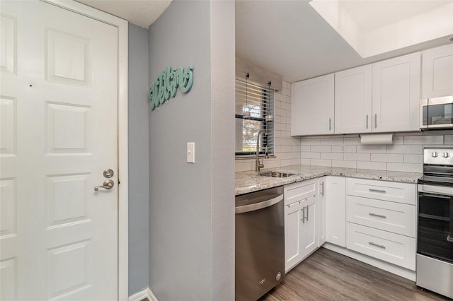 kitchen featuring sink, decorative backsplash, light stone countertops, white cabinetry, and stainless steel appliances