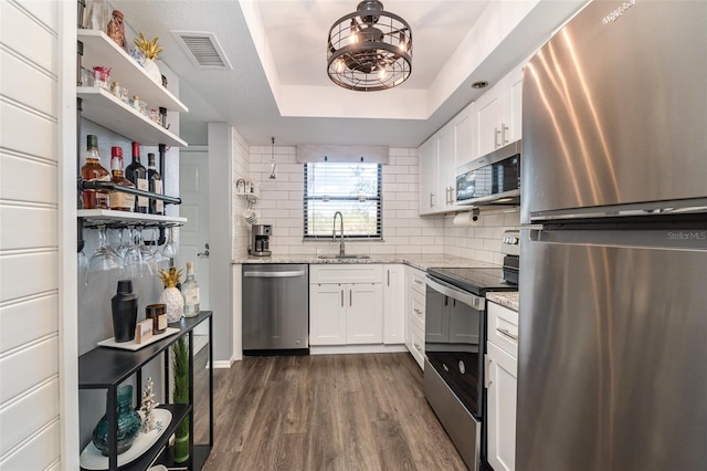 kitchen with a tray ceiling, sink, white cabinets, and appliances with stainless steel finishes