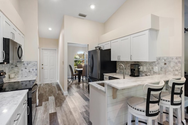 kitchen featuring kitchen peninsula, black range with electric stovetop, white cabinetry, and a breakfast bar