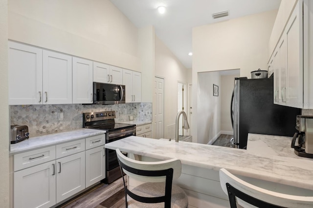 kitchen featuring tasteful backsplash, light stone countertops, white cabinets, and appliances with stainless steel finishes