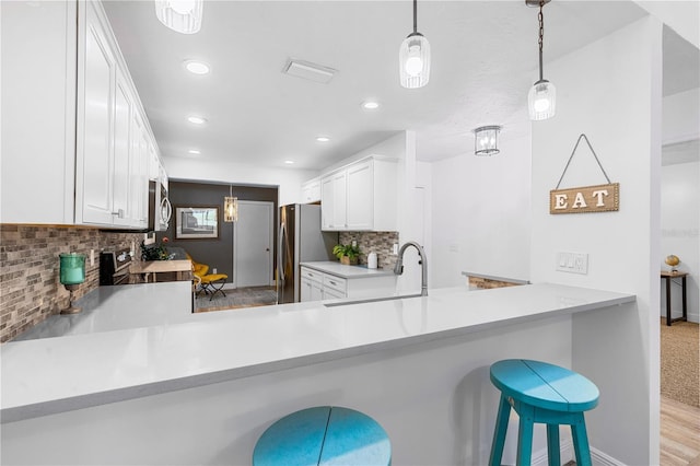 kitchen with stainless steel appliances, a kitchen breakfast bar, kitchen peninsula, decorative light fixtures, and white cabinets