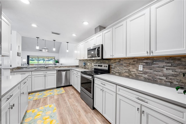 kitchen with white cabinets, appliances with stainless steel finishes, decorative light fixtures, light hardwood / wood-style floors, and kitchen peninsula