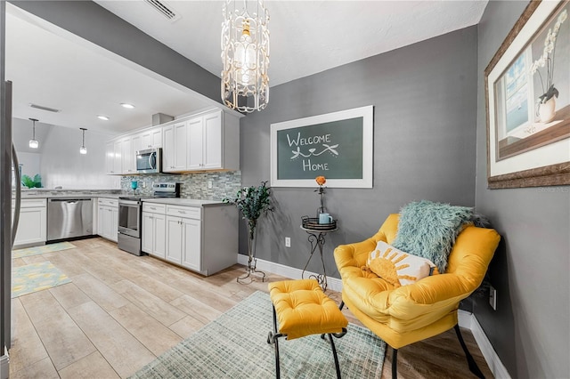 kitchen with backsplash, white cabinets, hanging light fixtures, light wood-type flooring, and appliances with stainless steel finishes