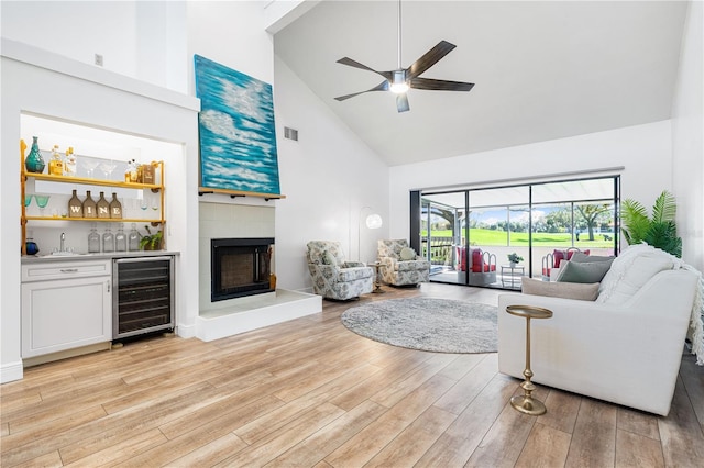 living room featuring ceiling fan, beverage cooler, high vaulted ceiling, indoor wet bar, and light hardwood / wood-style floors