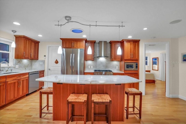 kitchen with appliances with stainless steel finishes, wall chimney exhaust hood, sink, a center island, and hanging light fixtures