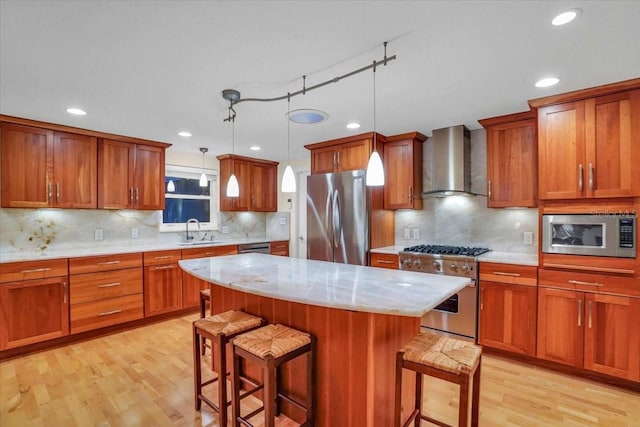 kitchen with a kitchen bar, stainless steel appliances, sink, wall chimney range hood, and hanging light fixtures