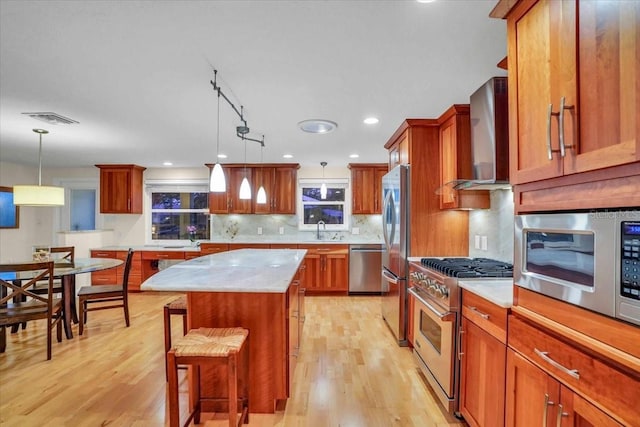 kitchen featuring pendant lighting, a breakfast bar, a center island, wall chimney exhaust hood, and appliances with stainless steel finishes