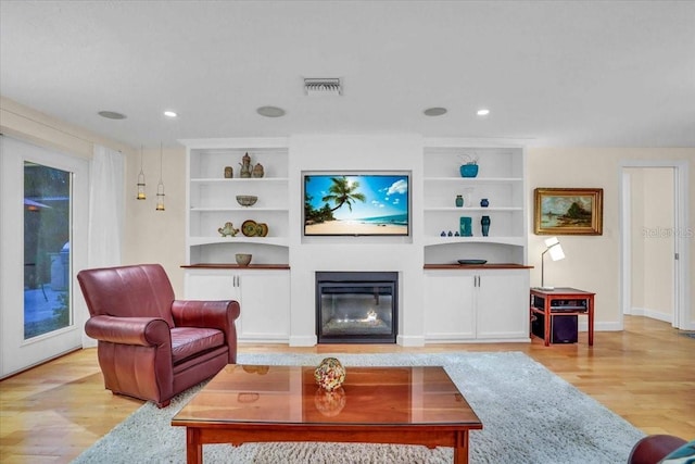 living room with built in shelves and light hardwood / wood-style flooring