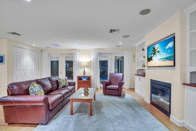 living room with built in features, light hardwood / wood-style floors, and french doors