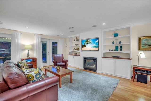 living room with built in shelves, french doors, and light hardwood / wood-style flooring