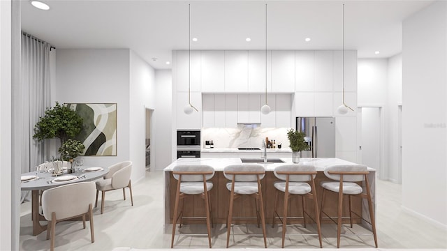 kitchen with a breakfast bar, decorative backsplash, an island with sink, white cabinetry, and stainless steel refrigerator