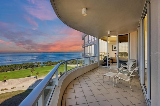 balcony at dusk featuring a water view