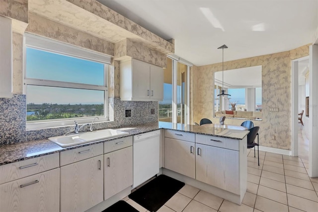 kitchen with kitchen peninsula, decorative backsplash, white dishwasher, sink, and hanging light fixtures