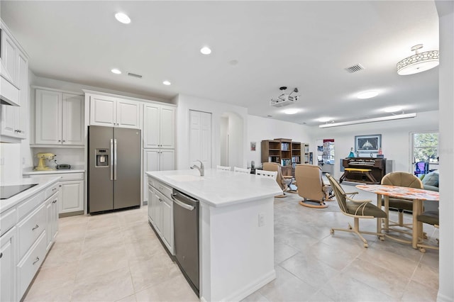 kitchen with sink, light tile patterned floors, a kitchen island with sink, white cabinets, and appliances with stainless steel finishes