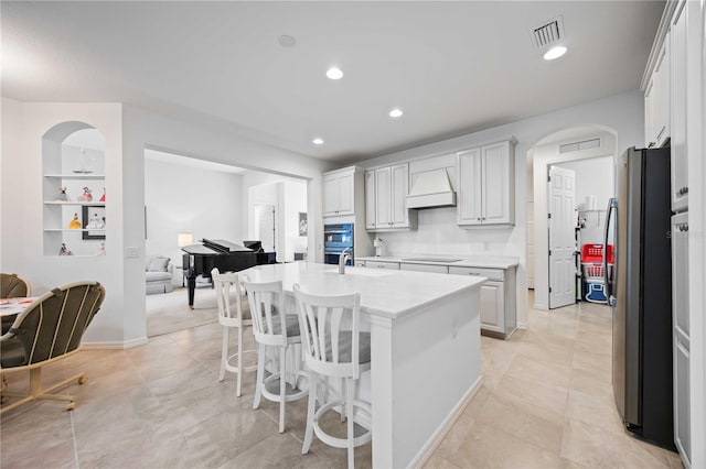 kitchen with white cabinetry, a kitchen island with sink, custom range hood, and appliances with stainless steel finishes