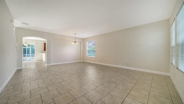 tiled spare room with a healthy amount of sunlight and an inviting chandelier