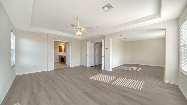 empty room featuring a raised ceiling, ceiling fan, light hardwood / wood-style flooring, and a textured ceiling