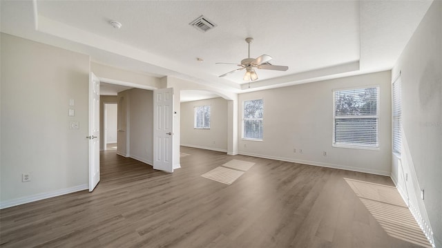 spare room featuring a textured ceiling, ceiling fan, dark wood-type flooring, and a tray ceiling