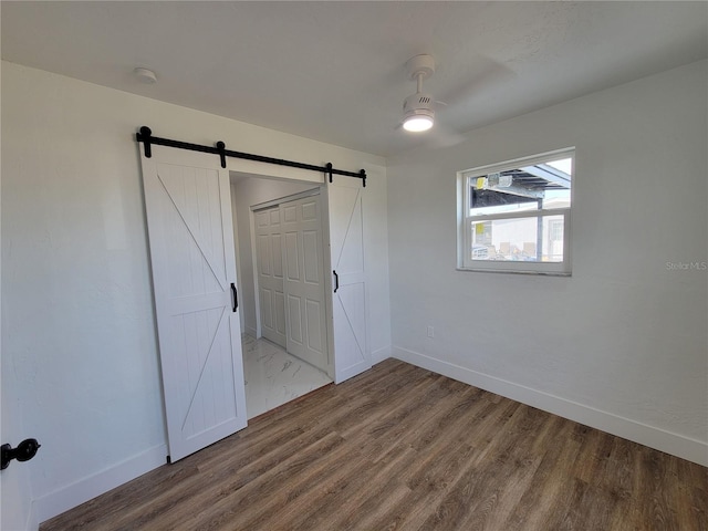 unfurnished bedroom with a barn door, ceiling fan, a closet, and hardwood / wood-style flooring