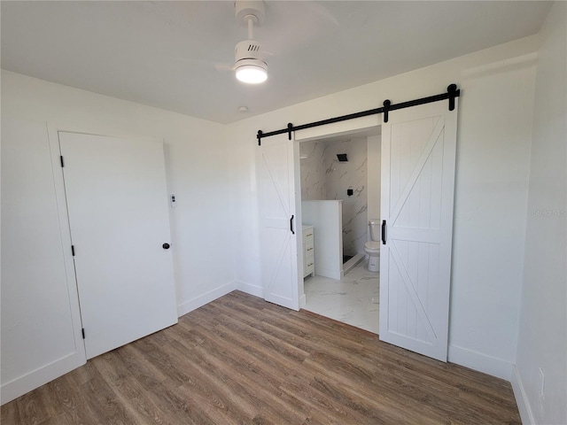 unfurnished bedroom featuring hardwood / wood-style flooring, ceiling fan, a barn door, and connected bathroom