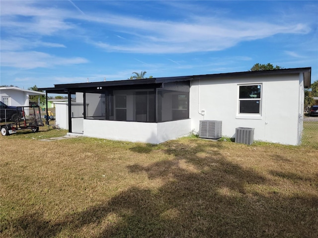 rear view of property with a lawn, a sunroom, central AC unit, and a carport