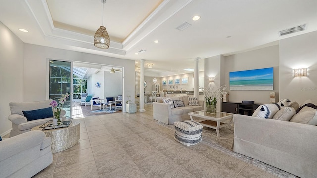 tiled living room featuring a tray ceiling, ceiling fan, decorative columns, and crown molding