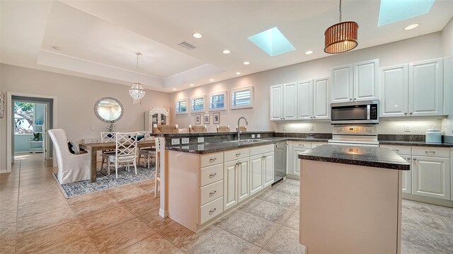 kitchen with a raised ceiling, sink, a skylight, appliances with stainless steel finishes, and decorative light fixtures