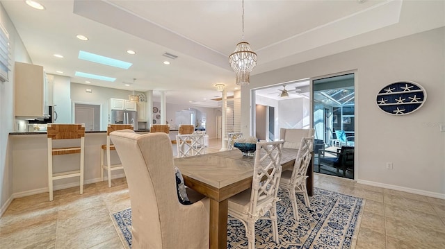 tiled dining space featuring ceiling fan with notable chandelier, a wealth of natural light, a tray ceiling, and a skylight