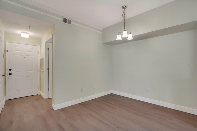 unfurnished room with hardwood / wood-style flooring, ornamental molding, and an inviting chandelier