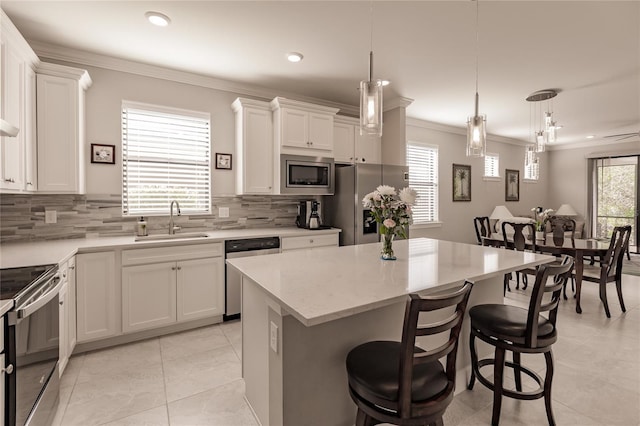 kitchen with sink, a center island, hanging light fixtures, white cabinets, and appliances with stainless steel finishes