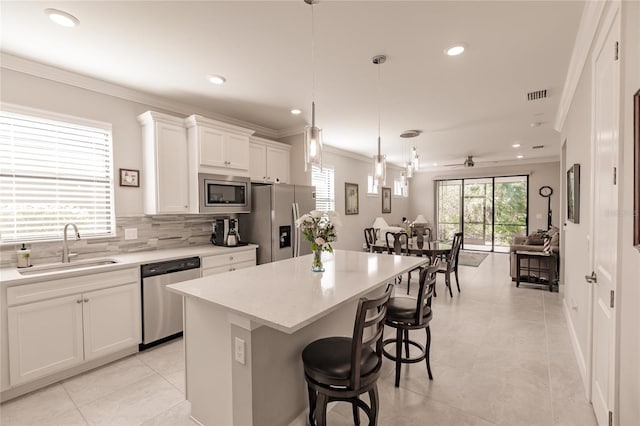 kitchen featuring stainless steel appliances, sink, white cabinetry, a kitchen island, and hanging light fixtures